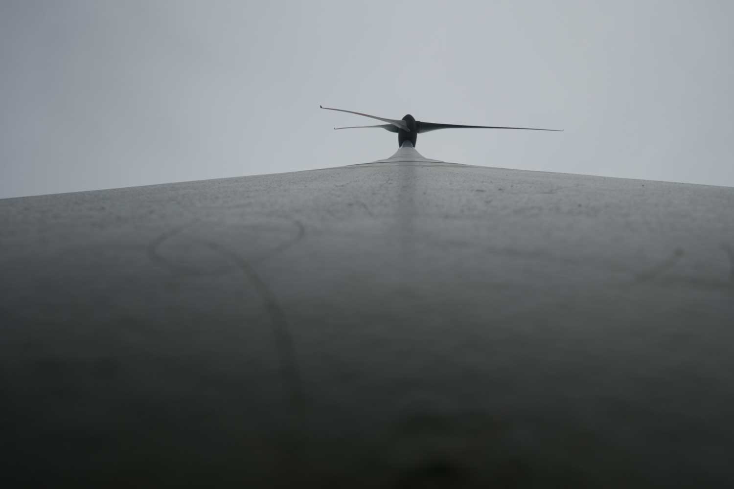 Upward view of airplane wingtip against a cloudy sky, highlighting aerodynamic design and overcast conditions.