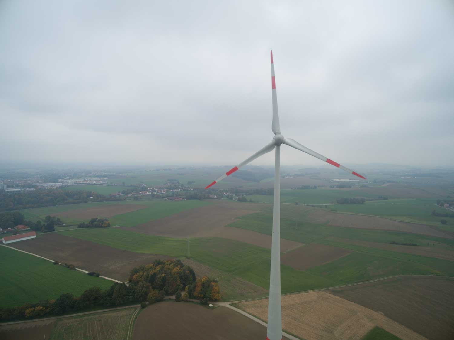 Aerial view of a wind turbine in a vast green and brown landscape under a cloudy sky.