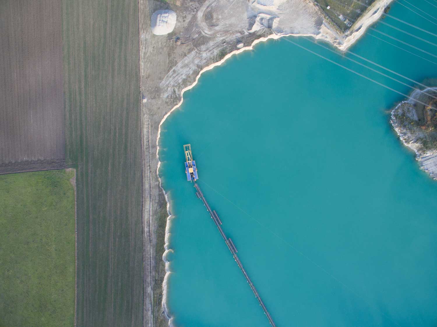 Aerial view of a turquoise lake beside agricultural fields, with a dock extending into the water.