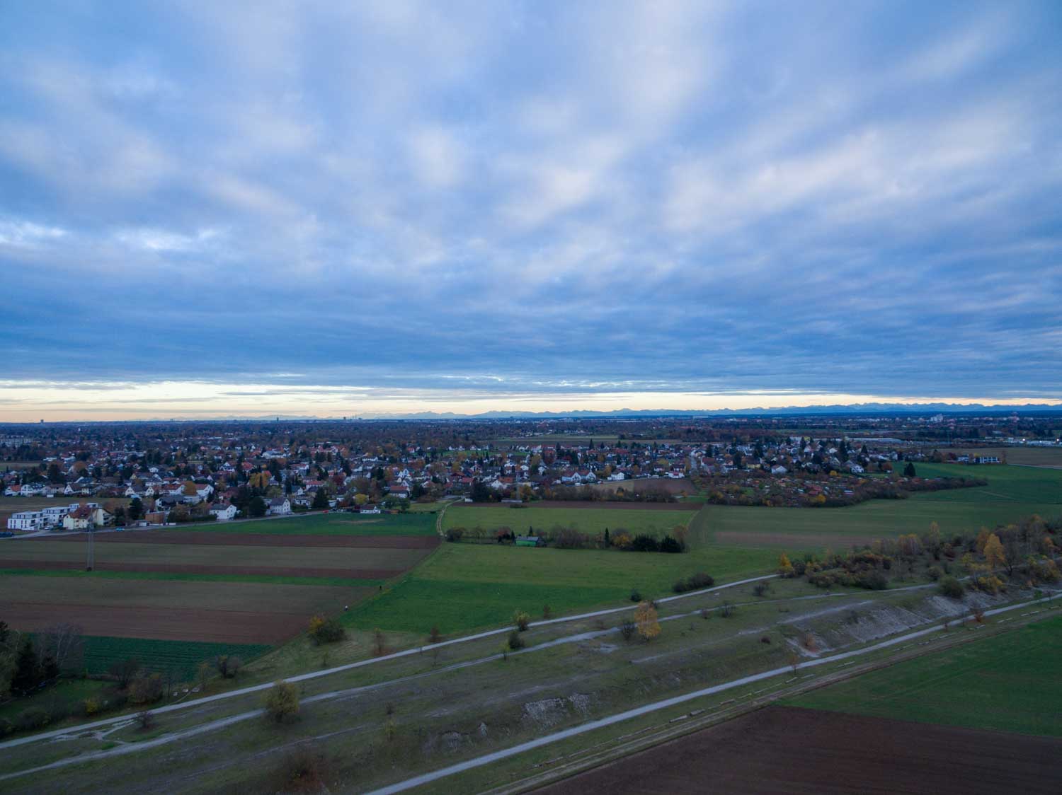 Aerial view of farmland and a small town with a cloudy sky at dusk, casting a serene blue tone over the landscape.