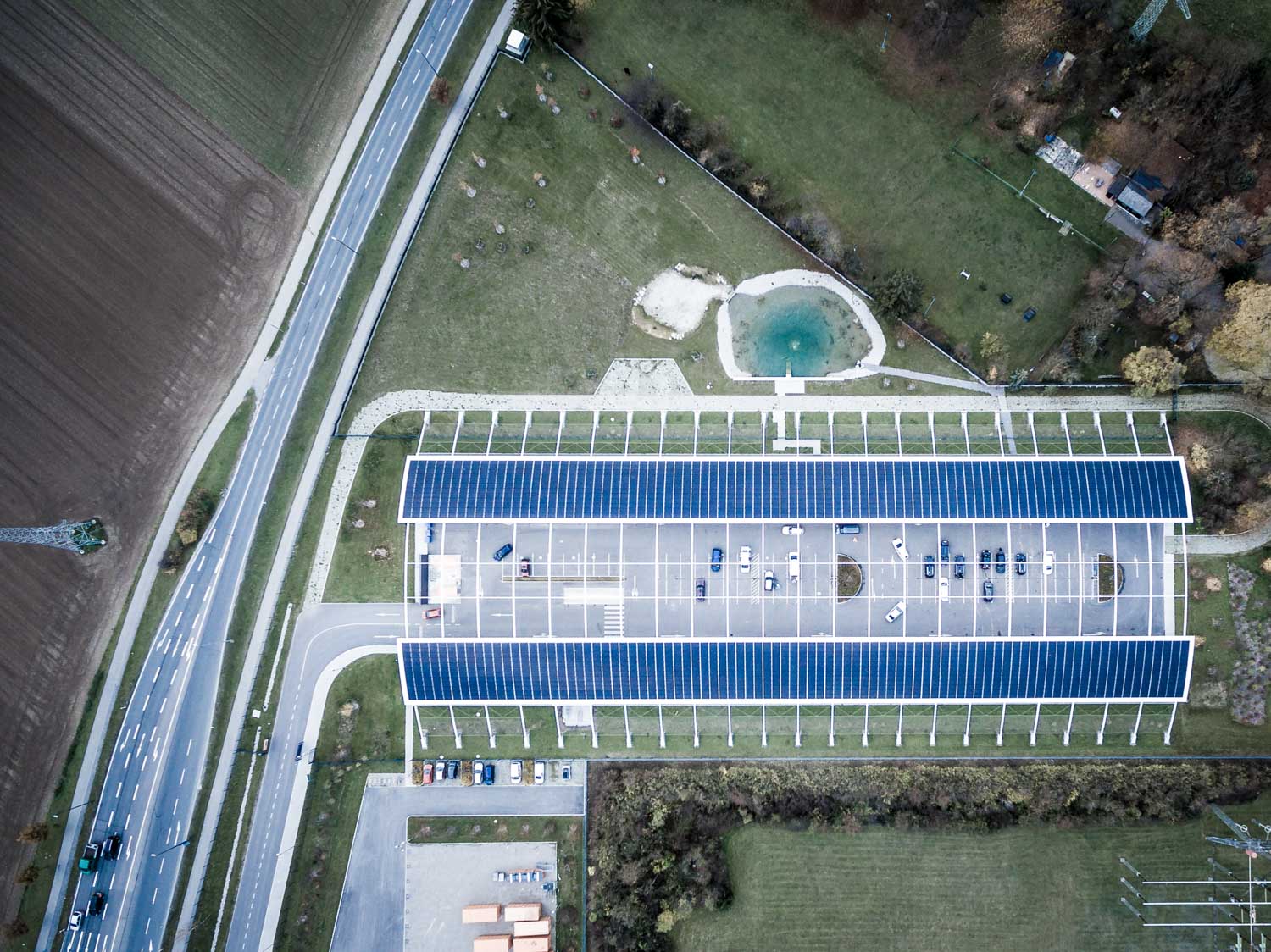 Aerial view of a solar-panel-covered parking lot next to a road and green landscape.