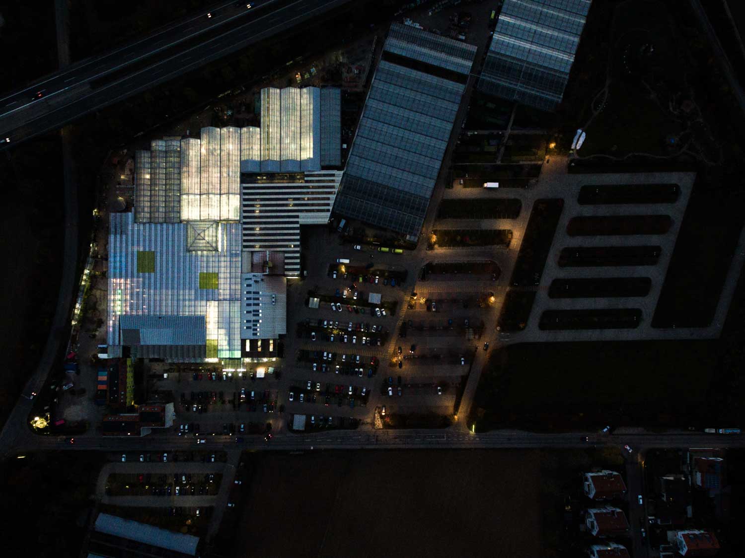 Aerial view of illuminated greenhouse complex with adjacent parking lots at night.