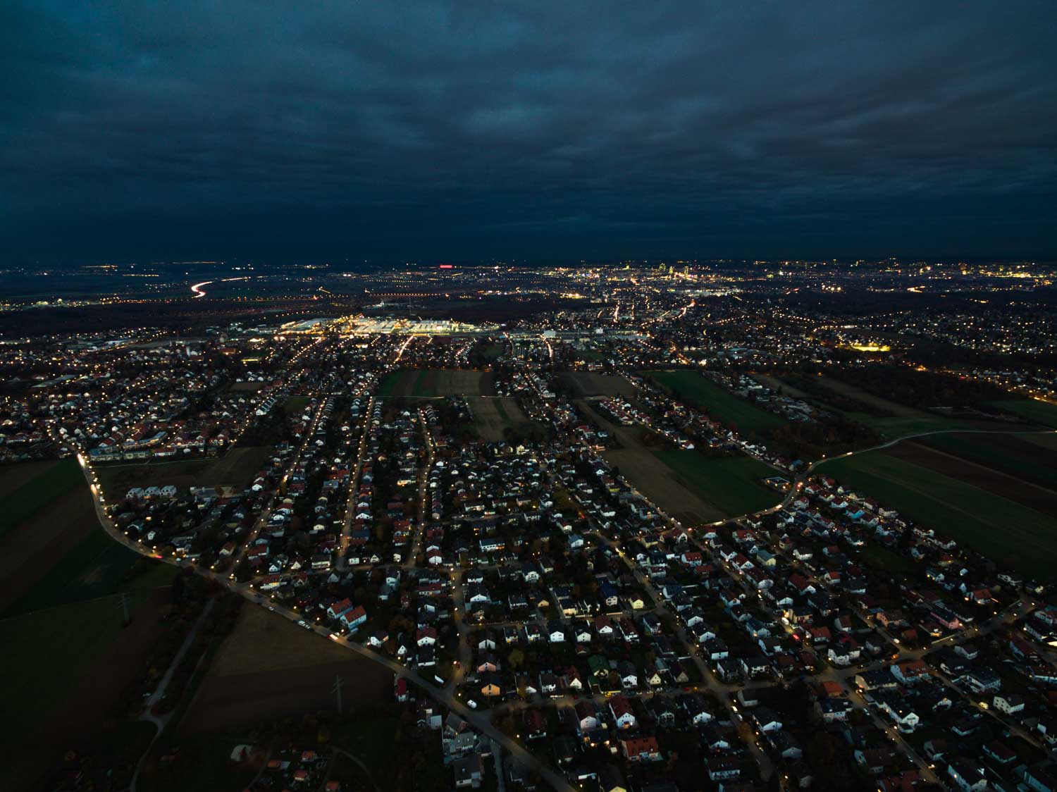 Aerial view of illuminated cityscape and suburbs at night, with roads and houses extending into the distance.