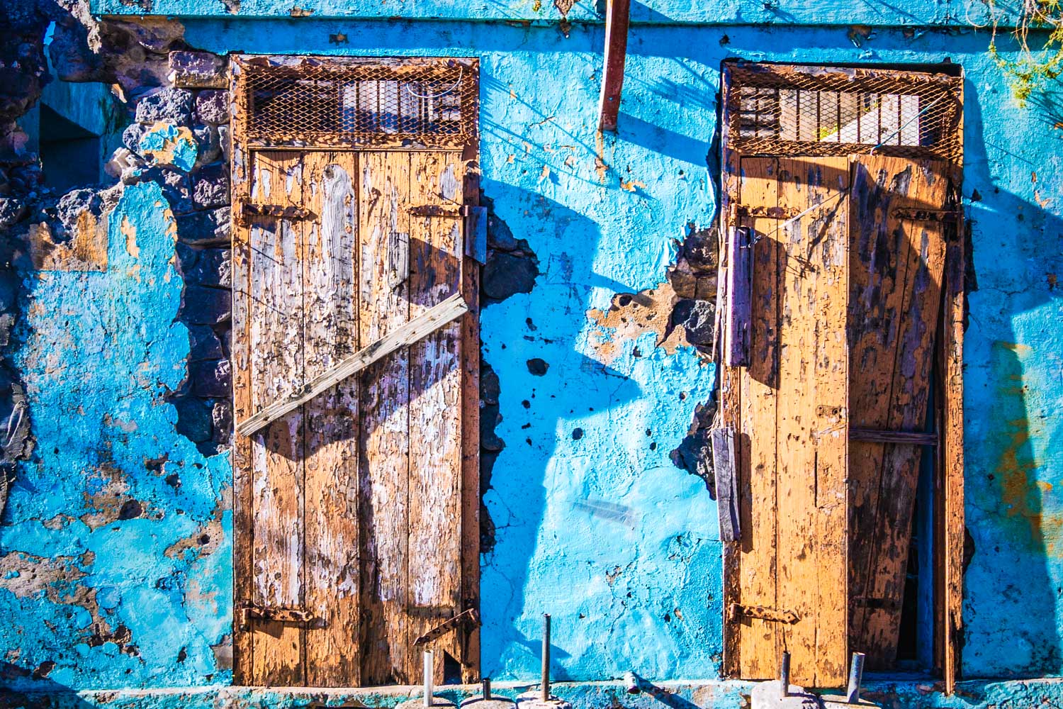 Two weathered wooden doors on a vibrant blue wall; rustic and aged appearance amidst stone textures.