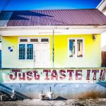 Caribbean Cruise – Father & Son Adventure 🌴 Yellow building with white door, red text Just TASTE IT! on wall, beside guesthouse sign. Bright sunny day.