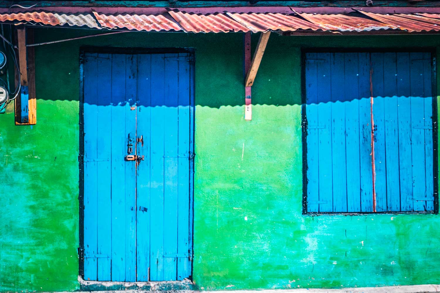 Blue door and window on vibrant green wall under rusted metal awning, creating a colorful, rustic facade.