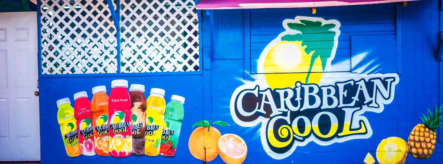 Colorful Caribbean Cool juice bottles painted on a vibrant blue wall with fruit and tropical designs.