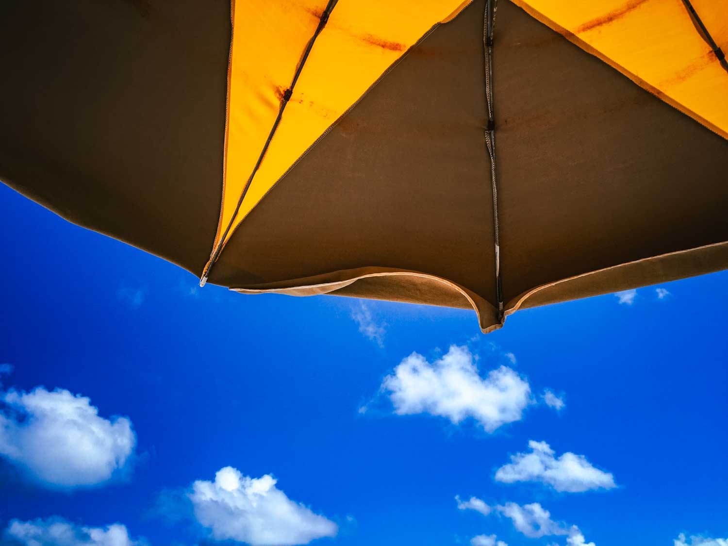 Yellow and brown beach umbrella against a clear blue sky with fluffy white clouds.
