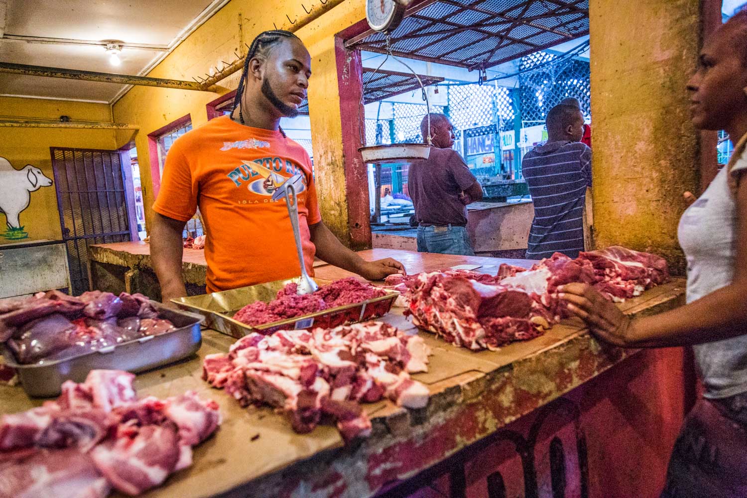 Butcher in an orange shirt selling fresh meat at a vibrant local market.