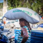 Caribbean Cruise – Island Hopping from Jamaica to Belize 🌴 Man carrying large sack labeled Rosario Superior on head by truck in busy street.