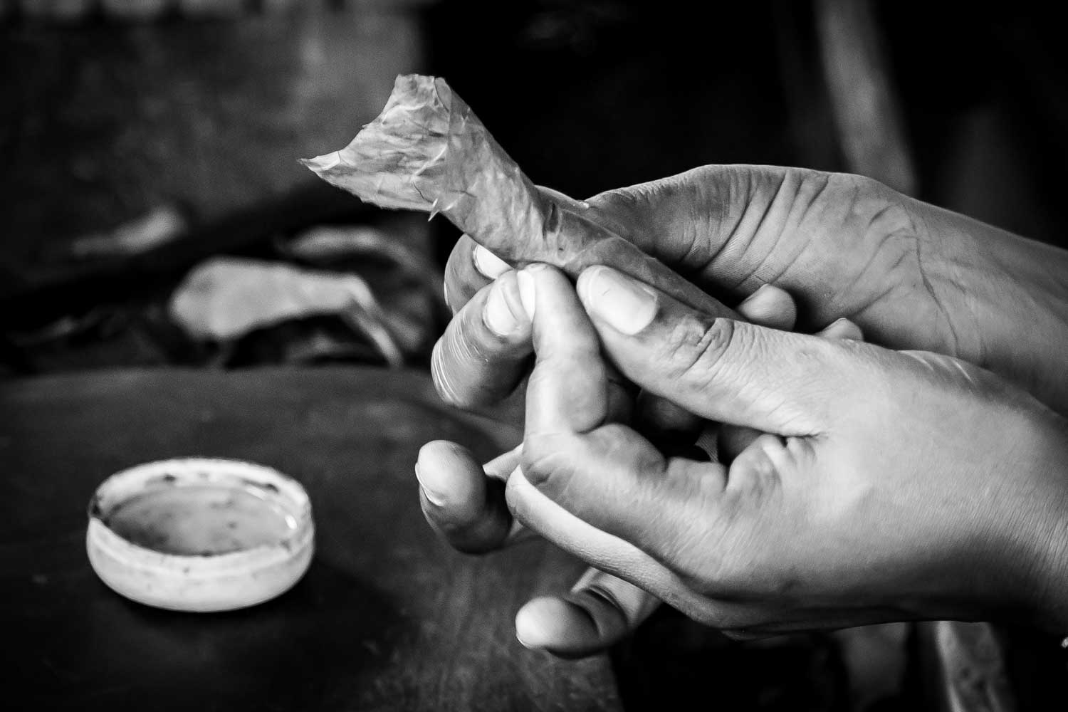 Close-up of hands rolling a traditional cigar with a leaf in black and white.
