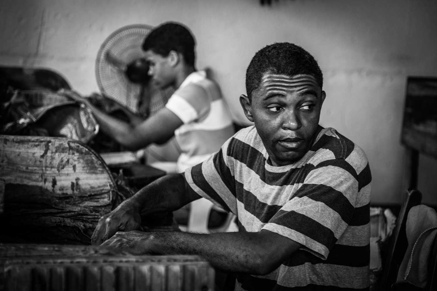 Two men working with machinery, one in focus wearing a striped shirt, the other blurred, in a workshop setting.