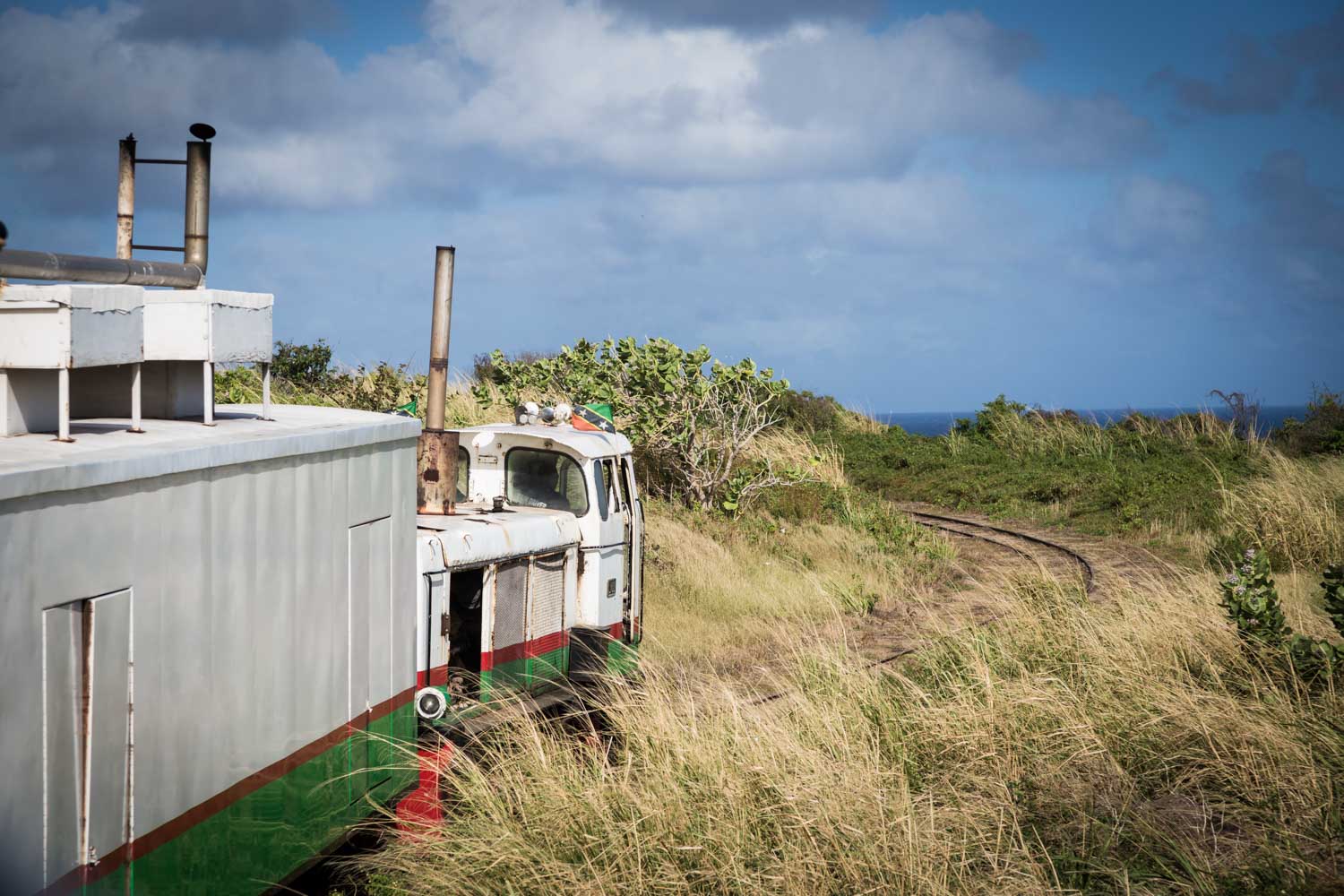 Vintage train on a scenic grassy track with ocean view in the background under a cloudy sky.