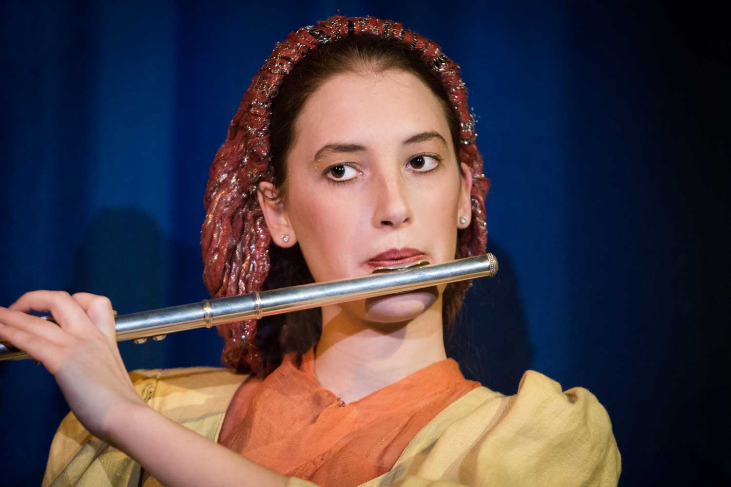 Young woman performing on a flute with a blue background.