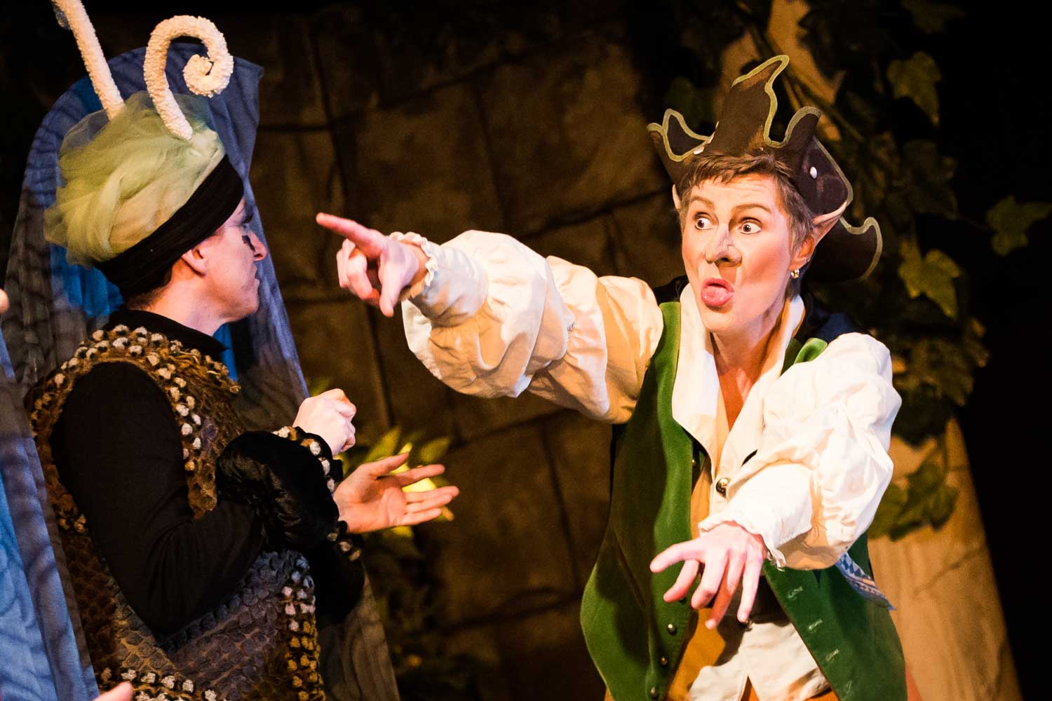 Actors in whimsical costumes perform energetically in a vibrant stage play.