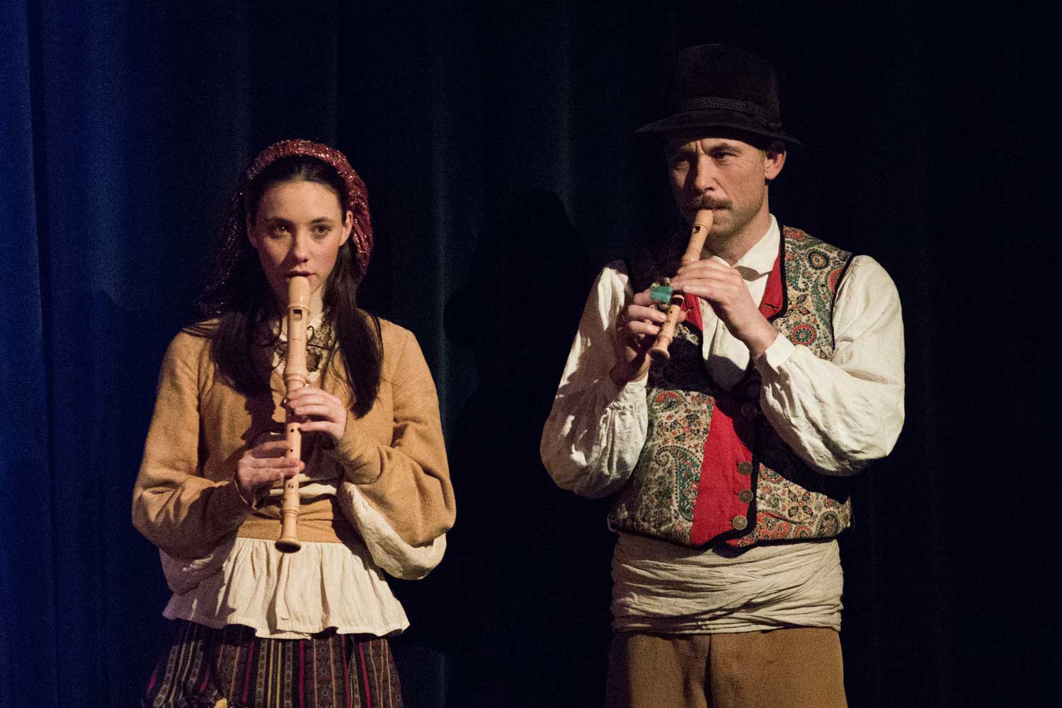 Two musicians in traditional attire playing recorders on stage.