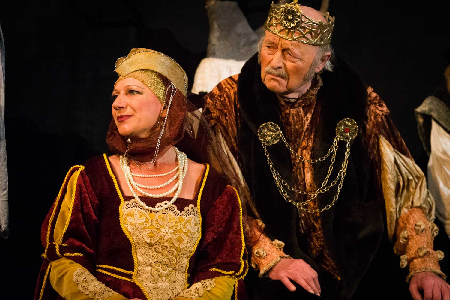 Actors in medieval costumes with crowns and jewelry performing on stage.
