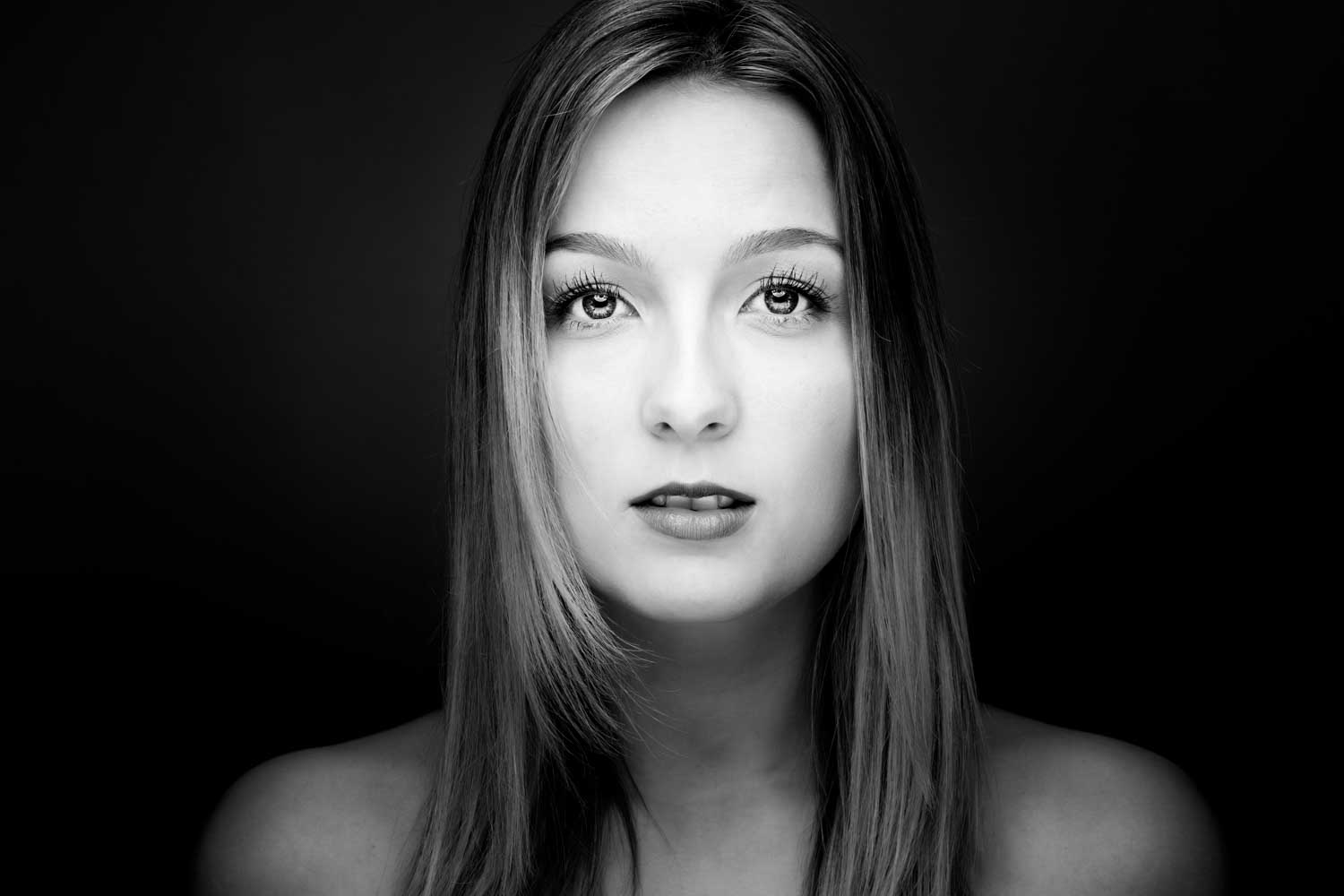 Black and white portrait of a woman with long hair, staring forward against a dark background.