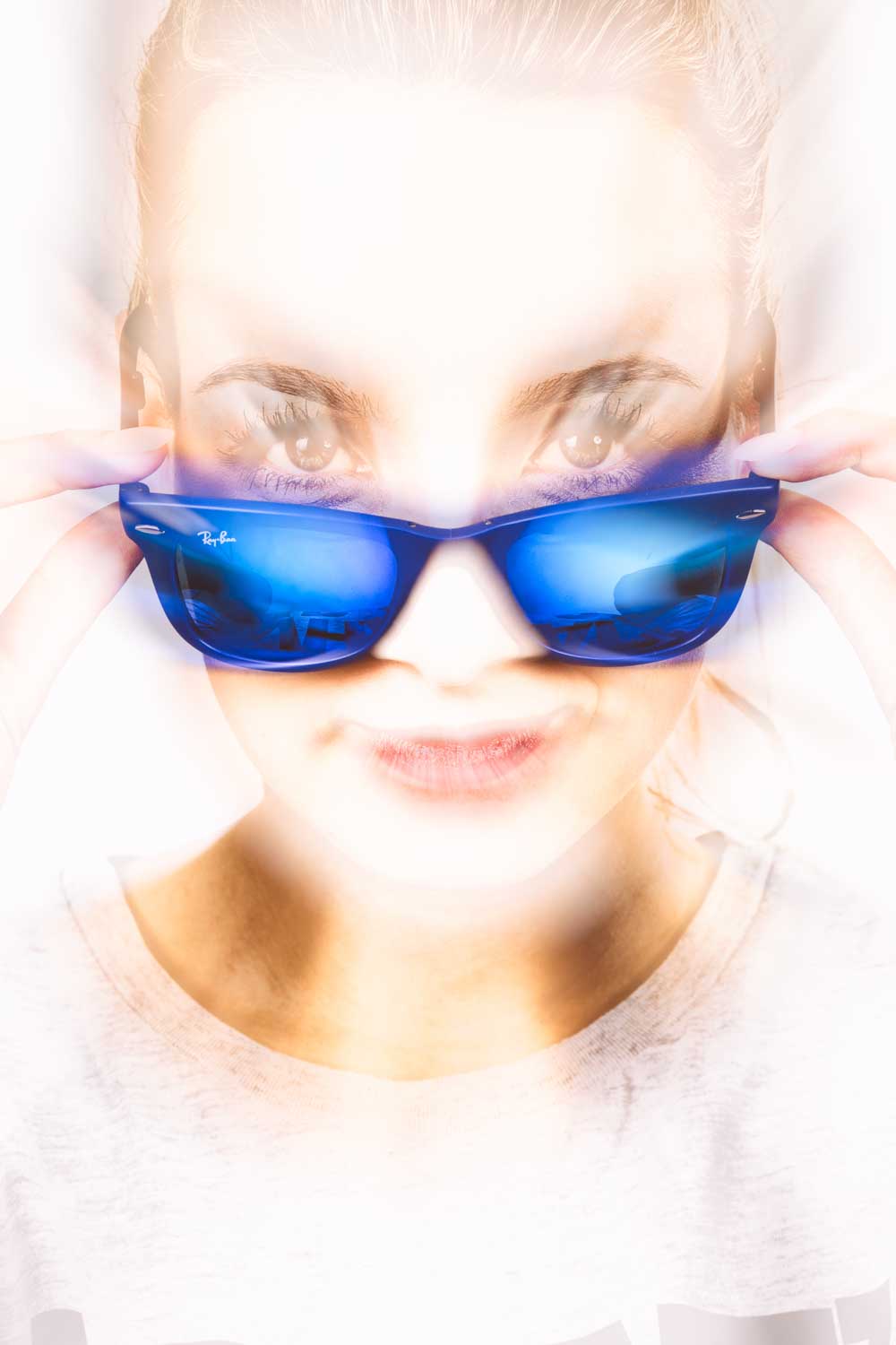 Woman wearing blue sunglasses, adjusting frames with both hands, intense light effect, partial face visible.