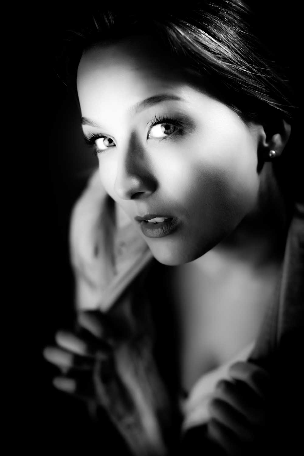 Black and white portrait of a woman with dramatic lighting, gazing forward, holding a jacket collar.