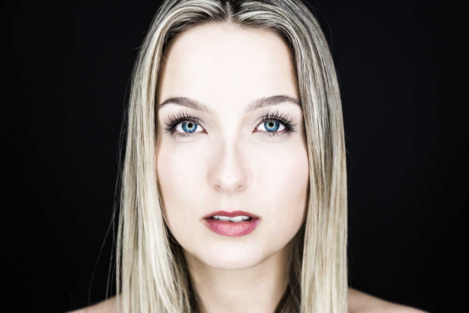 Close-up portrait of a woman with blue eyes and blonde hair against a black background.