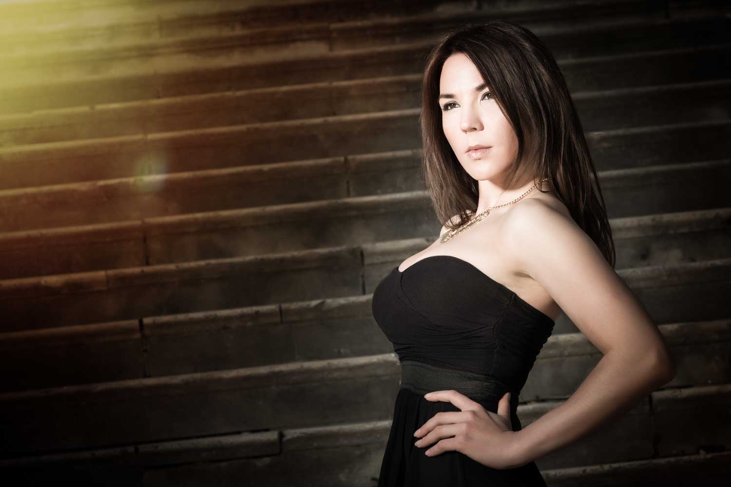Woman in black dress standing on stairs with sunlight in background.
