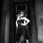 Stylish woman in black dress and sunglasses posing confidently between grand columns.