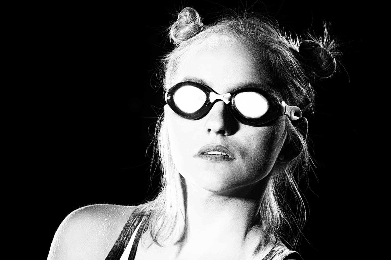 Black and white portrait of a woman in goggles with two buns hairstyle against a dark background.
