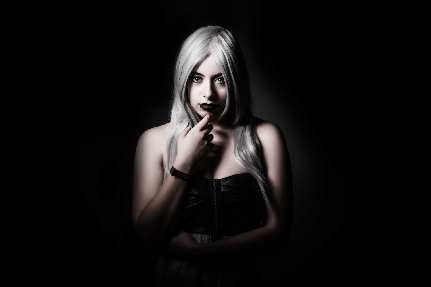 Mysterious woman with long silver hair and dark lipstick in dramatic lighting, wearing a black strapless top.