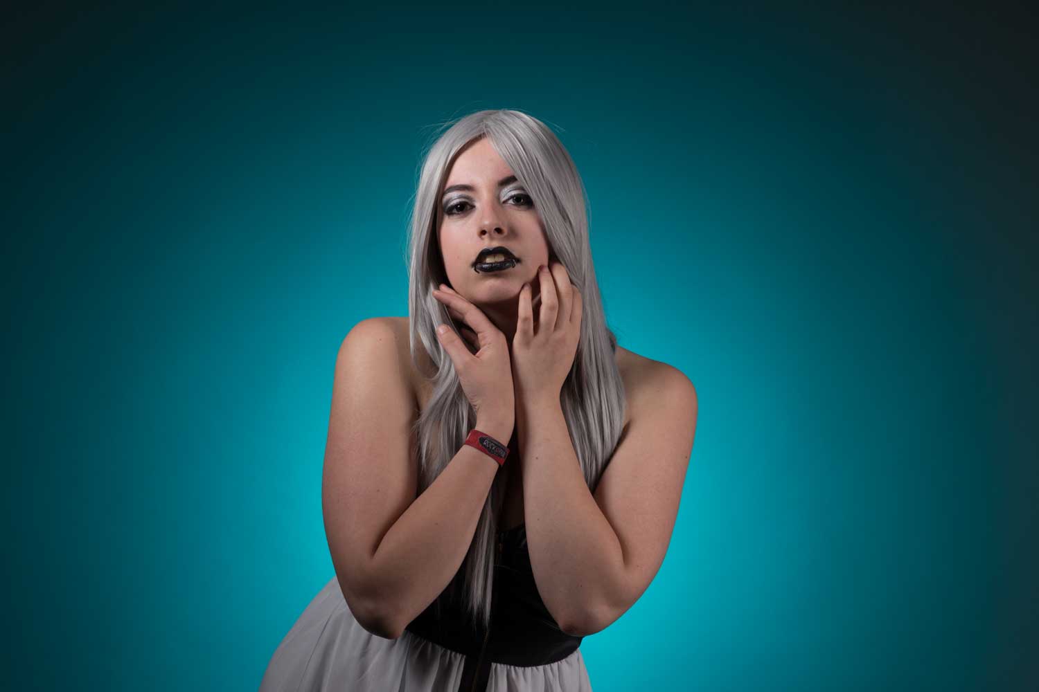 Person with long silver hair and dark makeup poses against a turquoise gradient background.