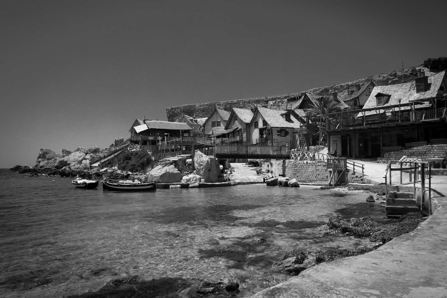 Black and white seaside village with wooden houses and boats on a rocky shoreline.