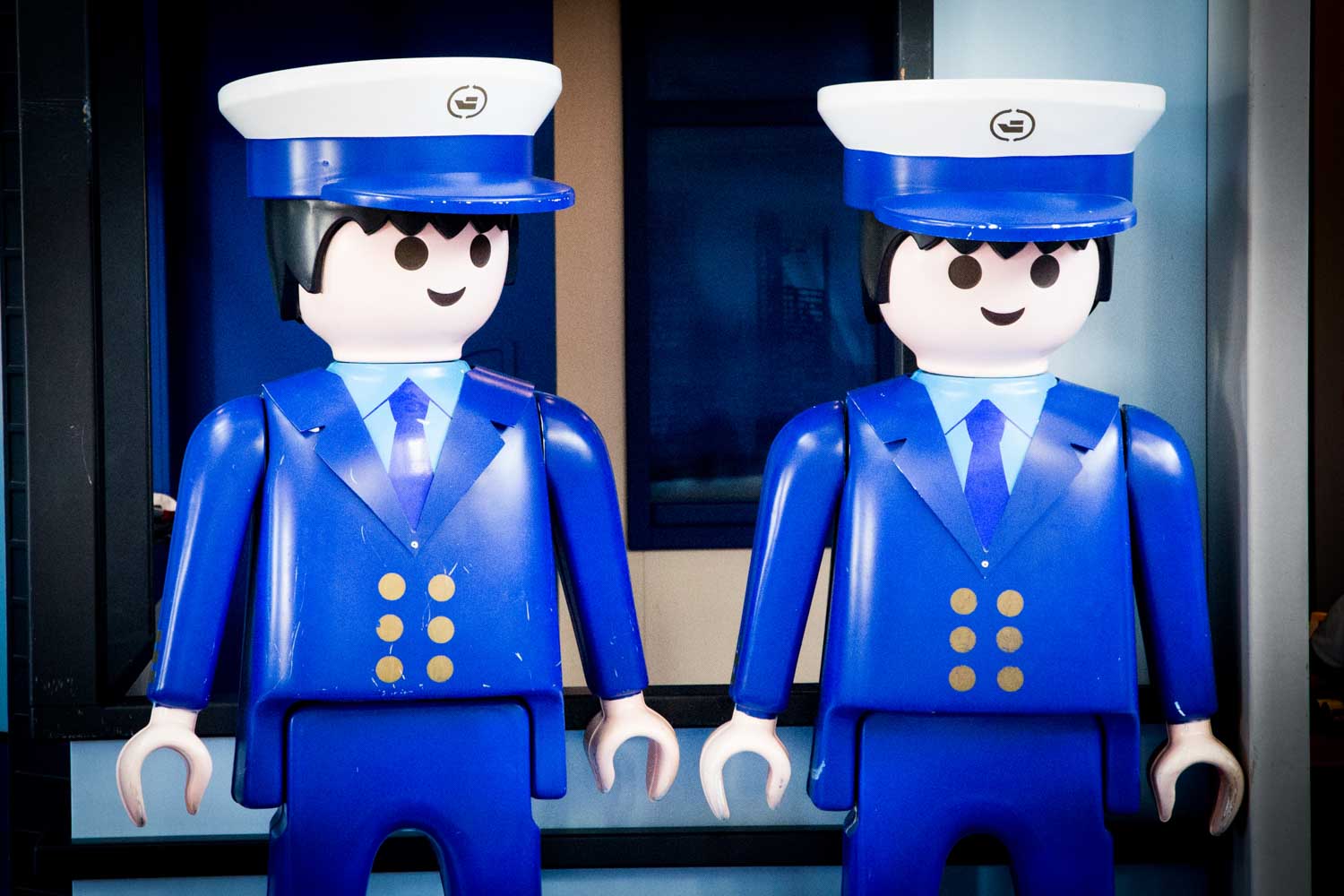 Two Playmobil figures dressed as captains in blue uniforms and white hats, standing together indoors.