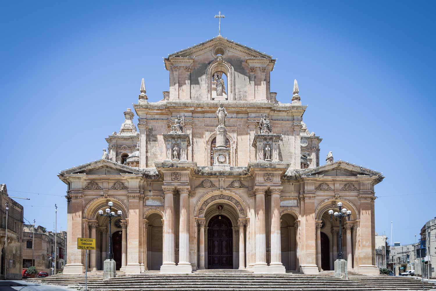 Historic stone cathedral with ornate columns and statues under a clear blue sky.