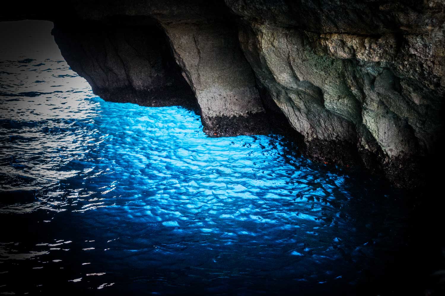 Blue glowing water inside a dark cave with rocky walls, creating a stunning natural light effect.