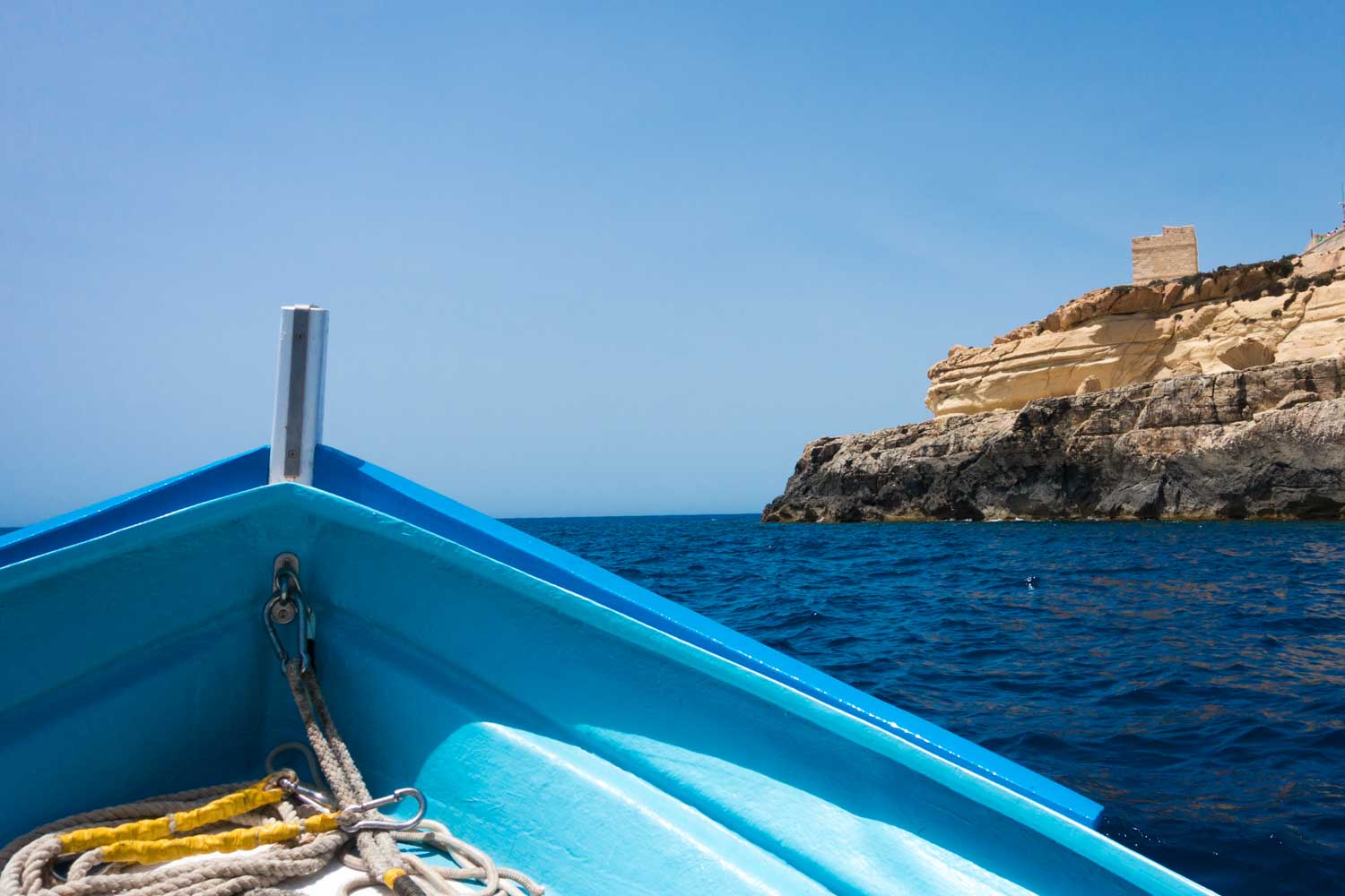 Blue boat on a clear sea near rocky cliffs under a bright sky.
