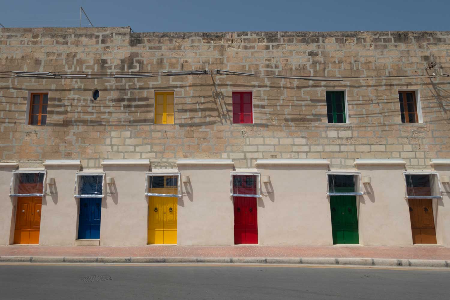 Colorful doors and windows on a stone building wall against a clear sky.