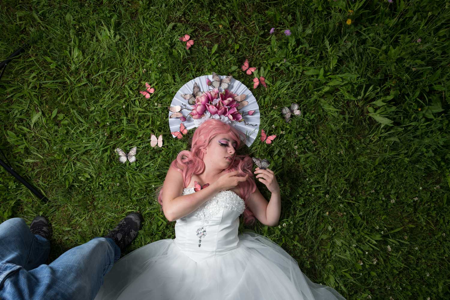 Woman in white dress with pink hair lies on grass, surrounded by butterflies and flowers.
