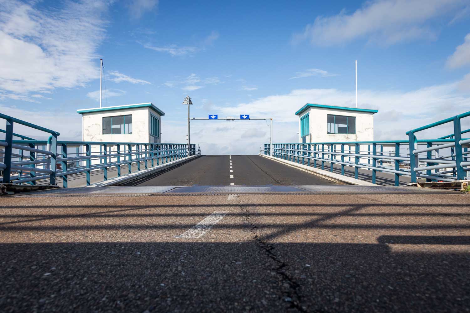 Elevated road bridge with two control booths, blue railings, and a clear sky.