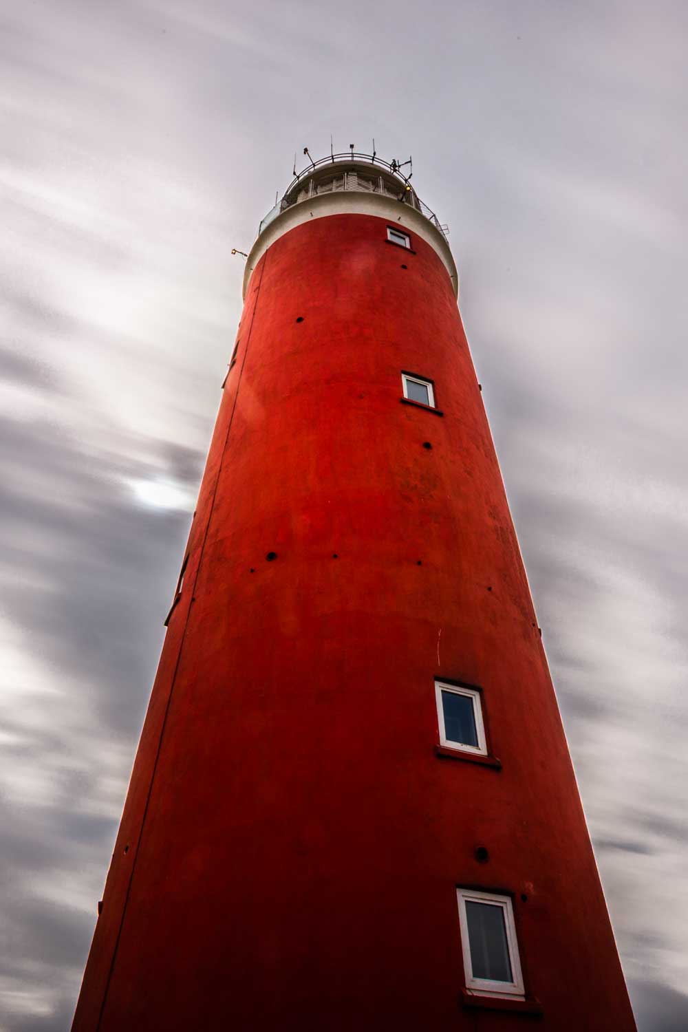 Tall red lighthouse against cloudy sky, low-angle view.