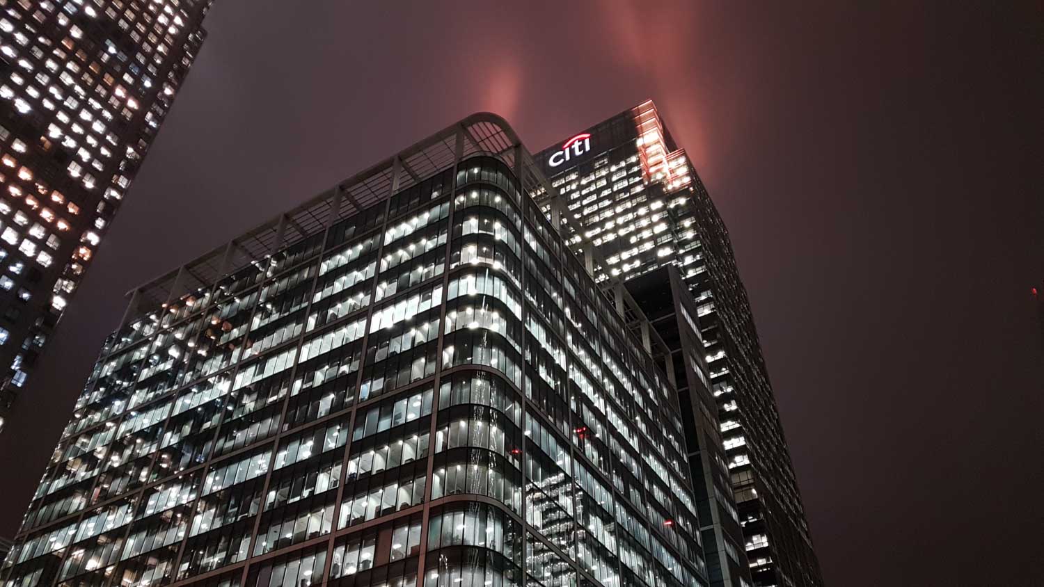 Illuminated city skyscrapers at night with Citi building and cloudy sky.