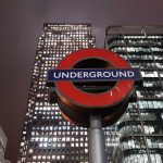 London Underground sign with skyscrapers in the background at night, including a Thomson Reuters building.