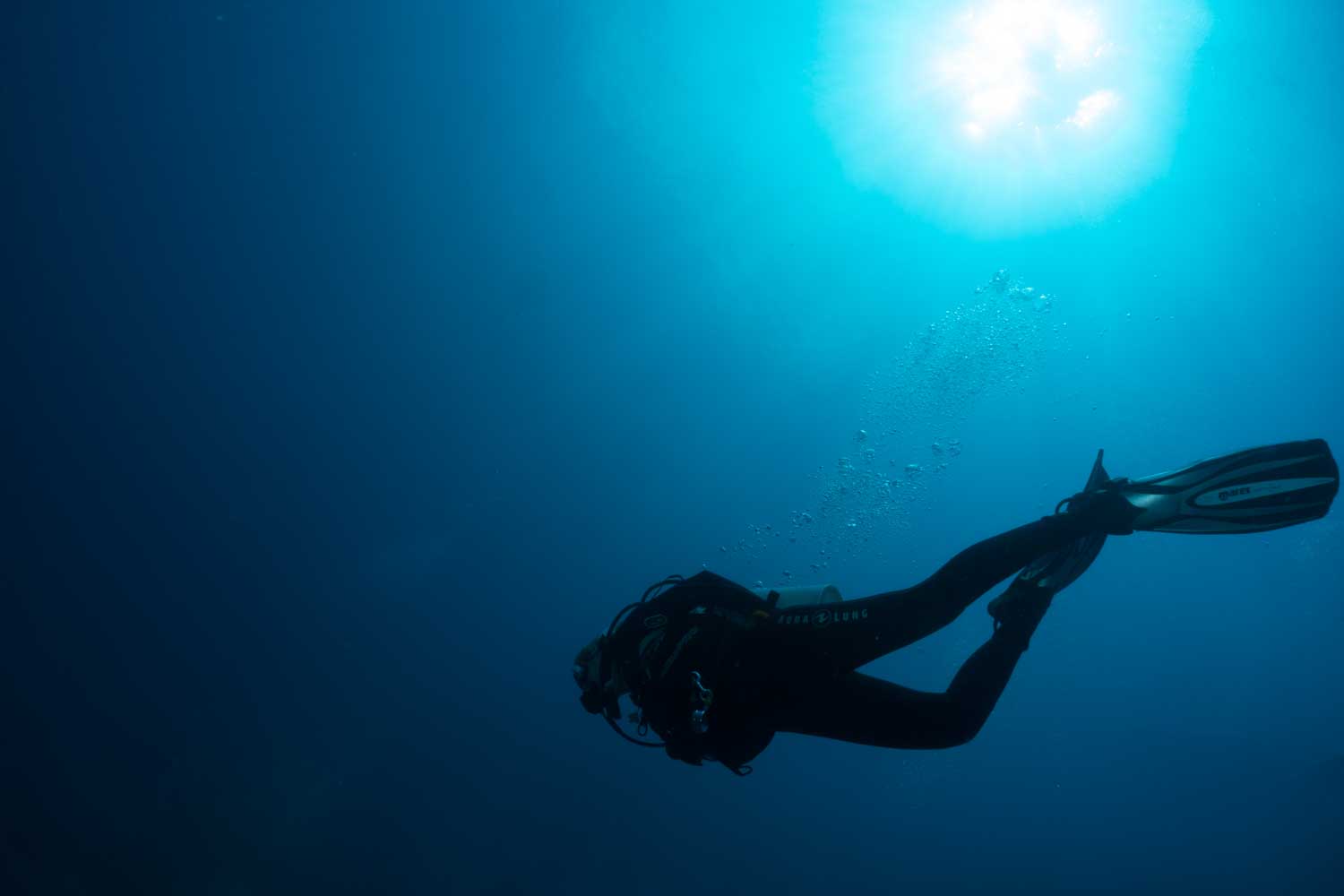 Scuba diver in deep blue ocean with sunlight filtering through water, surrounded by bubbles, exploring underwater.
