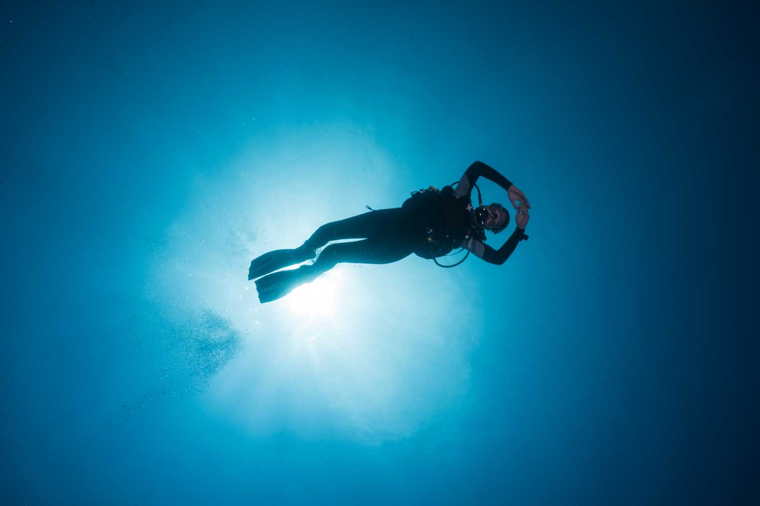 Scuba diver in ocean under sunlight, exploring underwater with gear and fins.