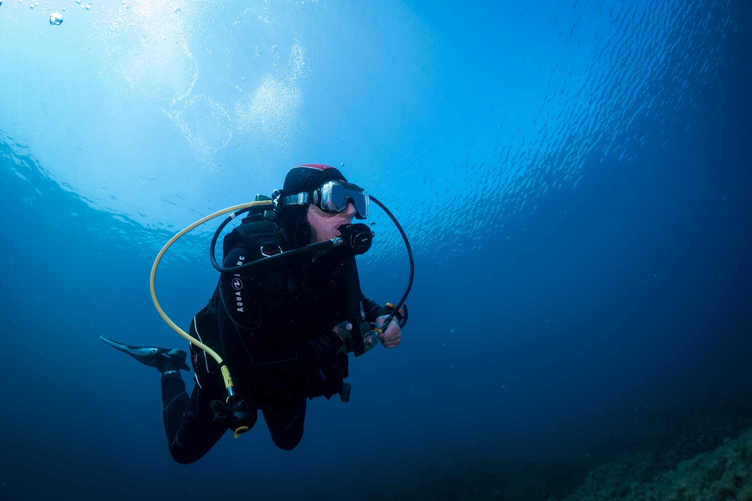 Diver with scuba gear exploring underwater, surrounded by clear blue ocean and sunlight filtering through the surface.