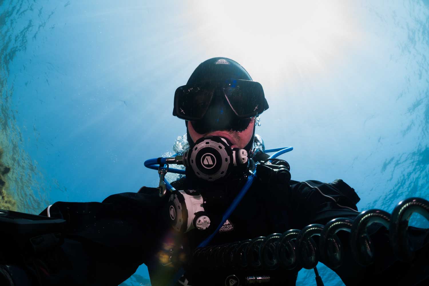 Scuba diver in full gear underwater, with sun rays piercing through the clear blue ocean above.