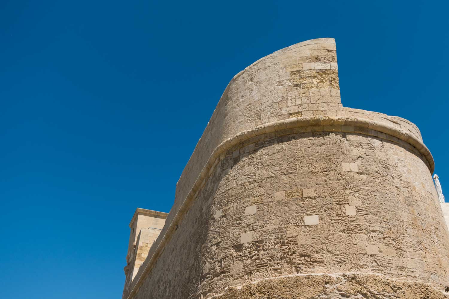 Historic stone building against a clear blue sky, showcasing textured architecture and smooth, curved walls.
