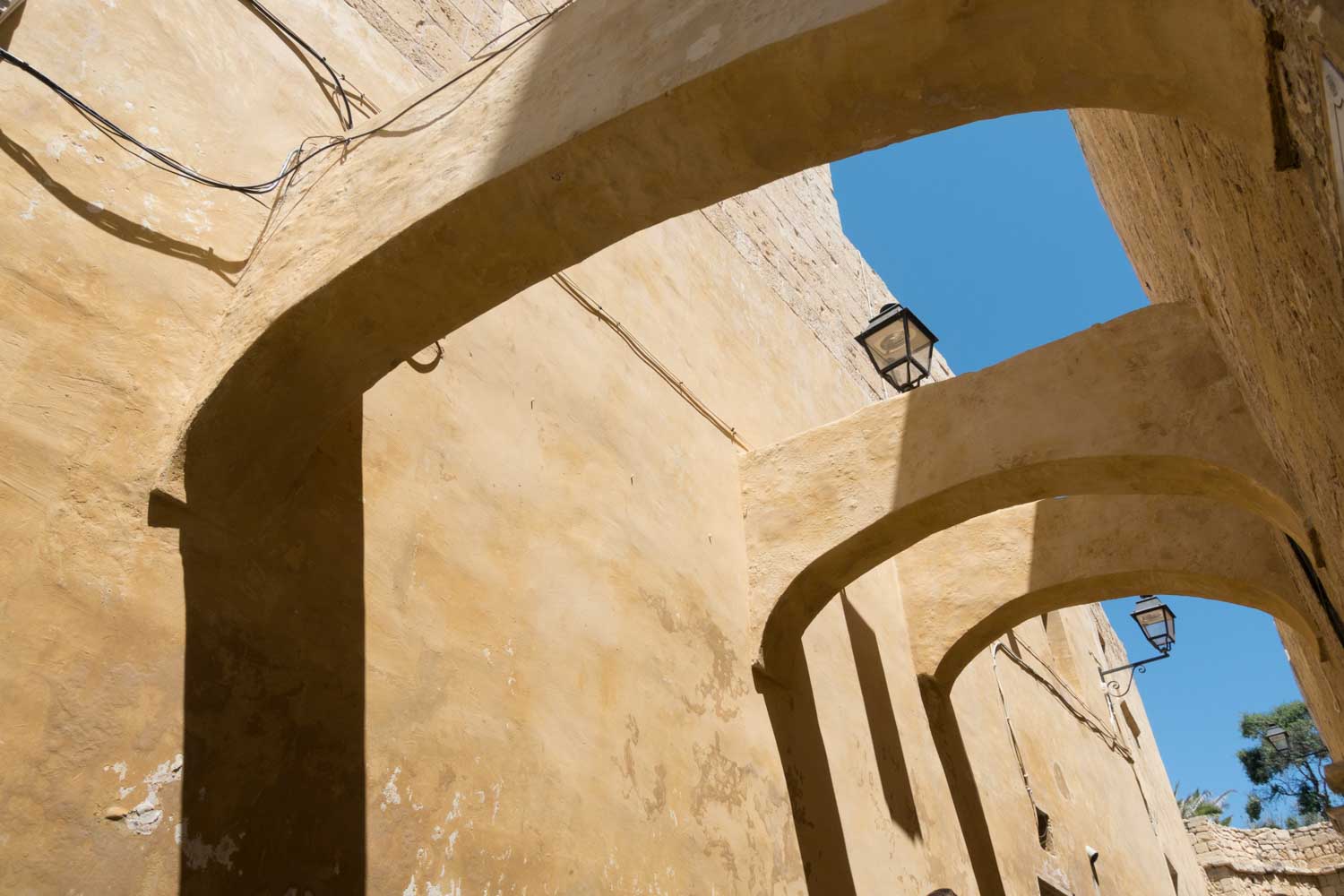Stone arches and walls with vintage lanterns under clear blue sky.