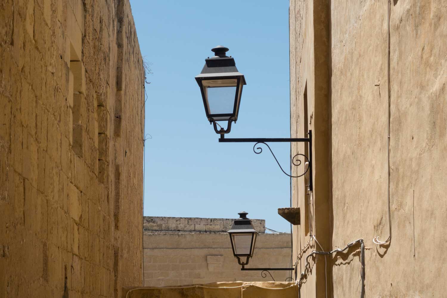 Rustic stone alley with vintage street lamps under a clear blue sky.