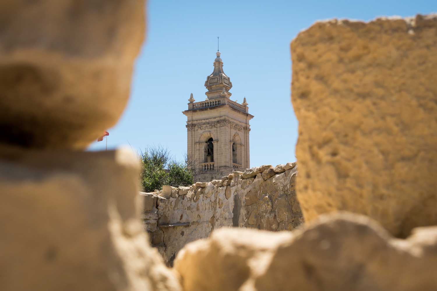 Historic stone church tower framed by ancient ruins under a clear blue sky.