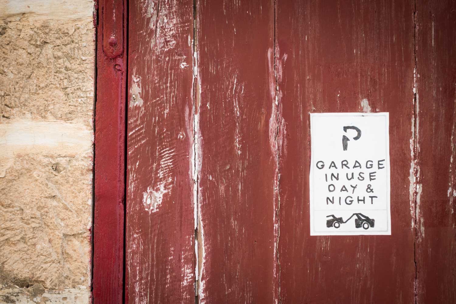 Weathered red garage door with Garage in use day & night sign, showing sketched towing cars.